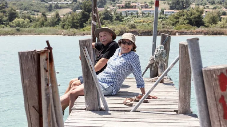 Relaxing elderly man and woman in hats and sunglasses enjoying time together while sitting on pier and looking at camera in Halkidiki, Greece Copyright: xInigoxCallesx